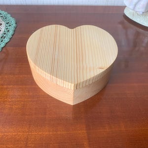 May include: A heart-shaped wooden box made of light-coloured wood. The box is closed and has a smooth, natural finish.