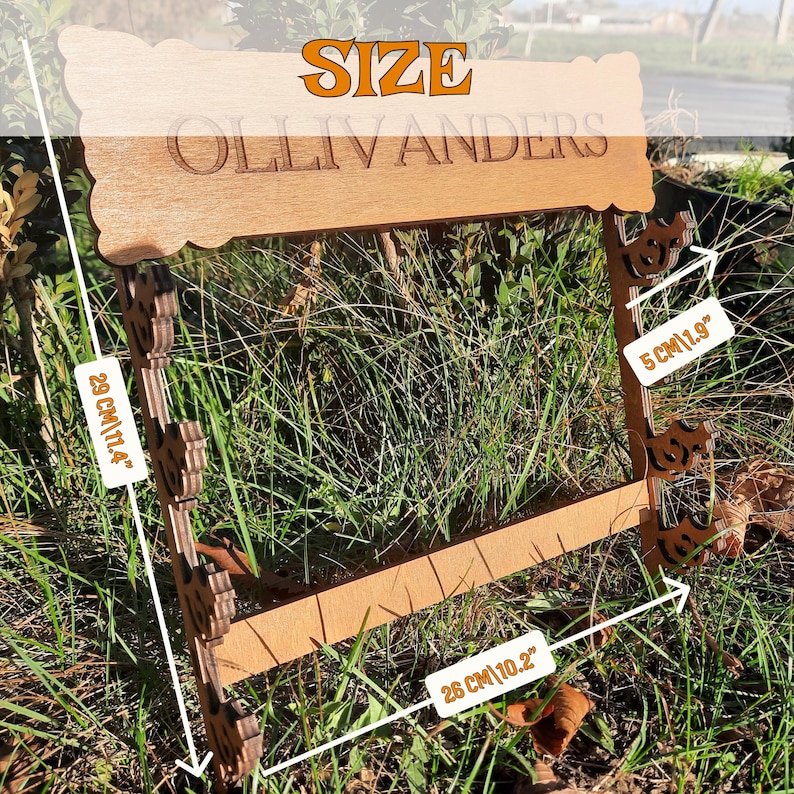Puede incluir: Se&ntilde;al de madera con el texto "Ollivanders" y la palabra "SIZE" encima. La se&ntilde;al mide 28 cm de ancho y 5 cm de alto. La se&ntilde;al est&aacute; sobre una superficie de hierba verde.