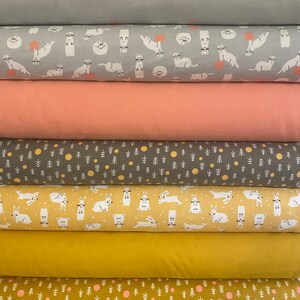 May include: A stack of fabric rolls in various colors and patterns. The top roll is solid gray, followed by a gray roll with white cartoon otters. Below are solid peach, gray with white trees and yellow circles, and yellow with white rabbits.