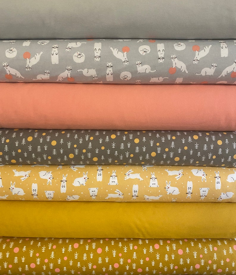 May include: A stack of fabric rolls in various colors and patterns. The top roll is solid gray, followed by a gray roll with white cartoon otters. Below are solid peach, gray with white trees and yellow circles, and yellow with white rabbits.