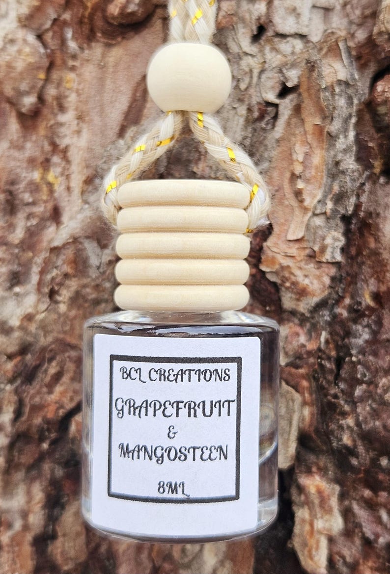 May include: A clear glass bottle with a wooden cap and a white label that reads "BCL Creations Grapefruit & Mangosteen 8ml". The bottle is hanging from a string with a wooden bead.