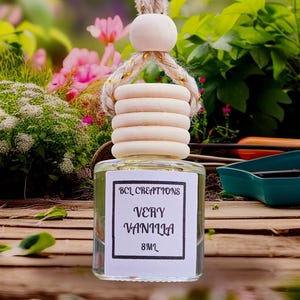 May include: A clear glass bottle with a wooden top and a label that reads "Very Vanilla 8ml". The bottle is suspended by a rope and wooden bead. The background features greenery and flowers.