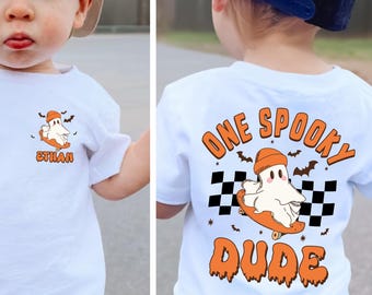 May include: White t-shirt with a Halloween-themed graphic. The front features a ghost on a skateboard with the name "Ethan". The back of the shirt says "One Spooky Dude" with a ghost and bats.