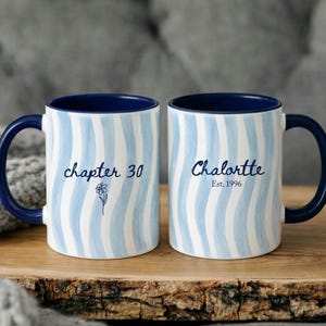 May include: Two white ceramic mugs with blue and white wavy stripes. One mug says "chapter 30" with a flower graphic, the other says "Chalortte Est. 1996". Both mugs have a dark blue interior and handle.