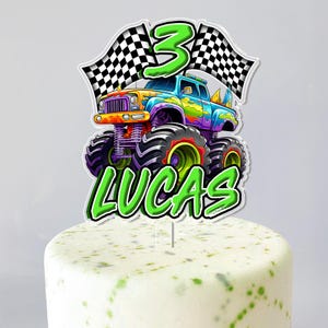 May include: A colorful monster truck cake topper with the number 3 and checkered flags. The name "LUCAS" is written in green. The truck is decorated with vibrant colors and sits atop a frosted cake.