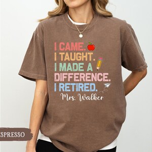 May include: A brown t-shirt with the text "I came. I taught. I made a difference. I retired. Mrs. Walker" in rainbow colors. The text is surrounded by a red apple, a pencil, and a paper airplane.