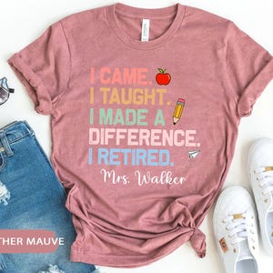 May include: Heather mauve t-shirt with the text "I came. I taught. I made a difference. I retired. Mrs. Walker" in colorful text with an apple and pencil graphic.