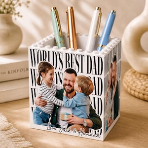 May include: A white square pen holder constructed from building blocks, featuring a printed photograph of a father with two children. The text "WORLD'S BEST DAD" is repeated in black, and the base includes the script text "Love, Jack & Hannah."