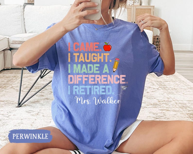 May include: A light blue t-shirt with the text "I came, I taught, I made a difference, I retired. Mrs. Walker" in rainbow colors. The text is surrounded by a red apple, a yellow pencil, and a paper airplane.