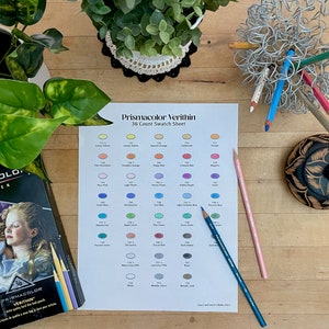 Może przedstawiać: Biała kartka papieru z kartą wzorów kolorów dla ołówków kolorowych Prismacolor Verithin. Karta przedstawia 36 różnych kolorów, każdy z nazwą i numerem. Na stole leżą trzy ołówki kolorowe: różowy, niebieski i turkusowy.