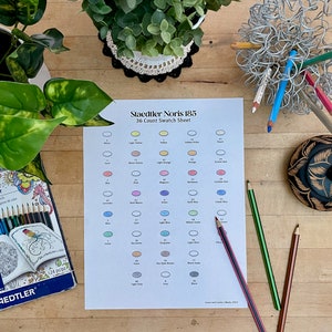 May include: A white sheet of paper with a color swatch chart for Staedtler Noris 185 colored pencils. The chart shows 36 different colors, each with a circle filled in with the corresponding color. The chart is labeled "Staedtler Noris 185" and "36 Count Swatch Sheet".
