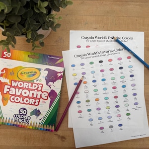 May include: A box of Crayola World's Favorite Colors 50 Colored Pencils sits on a wooden surface next to a color swatch sheet and two colored pencils. The box features a world map design and the Crayola logo.