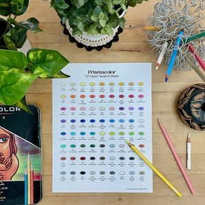 Może przedstawiać: Arkusz wzorników ołówków kolorowych Prismacolor w 72 kolorach, z różnymi kolorami, w tym żółtym, pomarańczowym, czerwonym, różowym, fioletowym, niebieskim, zielonym, brązowym, szarym i czarnym. Arkusz leży na drewnianym stole z puszką ołówków kolorowych Prismacolor Premier, rośliną i drucianym stojakiem na ołówki.