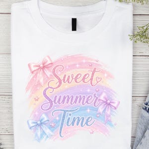 May include: A white t-shirt featuring a graphic print with the text Sweet Summer Time in glittery purple and blue script. The design includes pastel rainbow brushstrokes, small sparkling stars, and three light-colored bows in pink, purple, and blue.