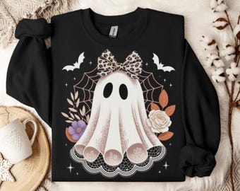 May include: Black sweatshirt featuring a white ghost design with a leopard print bow, spiderweb, and floral accents. The ghost has black oval eyes and a lace-trimmed bottom. Two white bats are above the ghost. A Halloween-themed graphic.