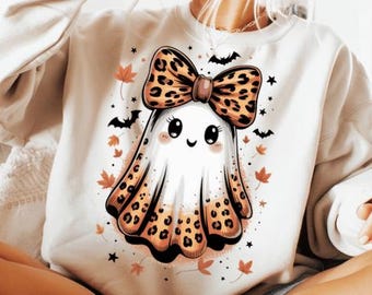 May include: White sweatshirt featuring a cute cartoon ghost with a leopard print bow and accents. The ghost has a smiling face and is surrounded by bats, stars, and autumn leaves. A fun and festive design for Halloween.