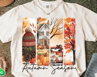 Può includere: T-shirt bianca con grafica a tema autunnale. Il design include un berretto di lana, pigne, una casa, zucche, un camion rosso e foglie autunnali. Le parole "Autumn Season" sono scritte in corsivo.
