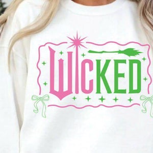 May include: White sweatshirt with the word "WICKED" in pink and green, with a star and broom graphic. The design is framed by a pink border with green accents, including bows and stars.