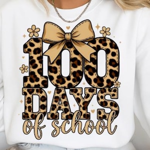May include: White sweatshirt with a leopard print design featuring the text "100 Days of School." The numbers and letters are in a brown and black leopard print pattern, with a tan bow and floral accents.