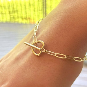 May include: A gold chain bracelet with a heart-shaped clasp. The bracelet is made of a thick, chunky chain.