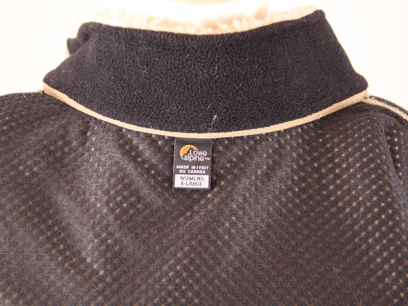 Pode incluir: Casaco de l&atilde; preto com forro de malha castanho e uma etiqueta castanha que diz "Lowe Alpine" e "Made in/Fait au Canada" e "Womens X Large".