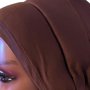 May include: A brown satin sleep cap with a smooth, silky texture. The cap is designed to protect hair while sleeping.