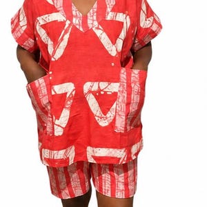 Könnte beinhalten: Rot-weiß gemustertes zweiteiliges Outfit. Das Oberteil hat einen V-Ausschnitt und kurze Ärmel mit zwei Vordertaschen. Die Shorts passen zum Muster des Oberteils. Das Outfit wird mit weißen Turnschuhen getragen.