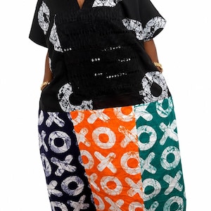 Pu&ograve; includere: Un abito a maniche corte con corpetto nero a motivi circolari bianchi e scollo a V. La gonna &egrave; divisa in tre pannelli verticali blu navy, arancione e verde, ciascuno decorato con un motivo bianco ripetuto a forma di XOXO.