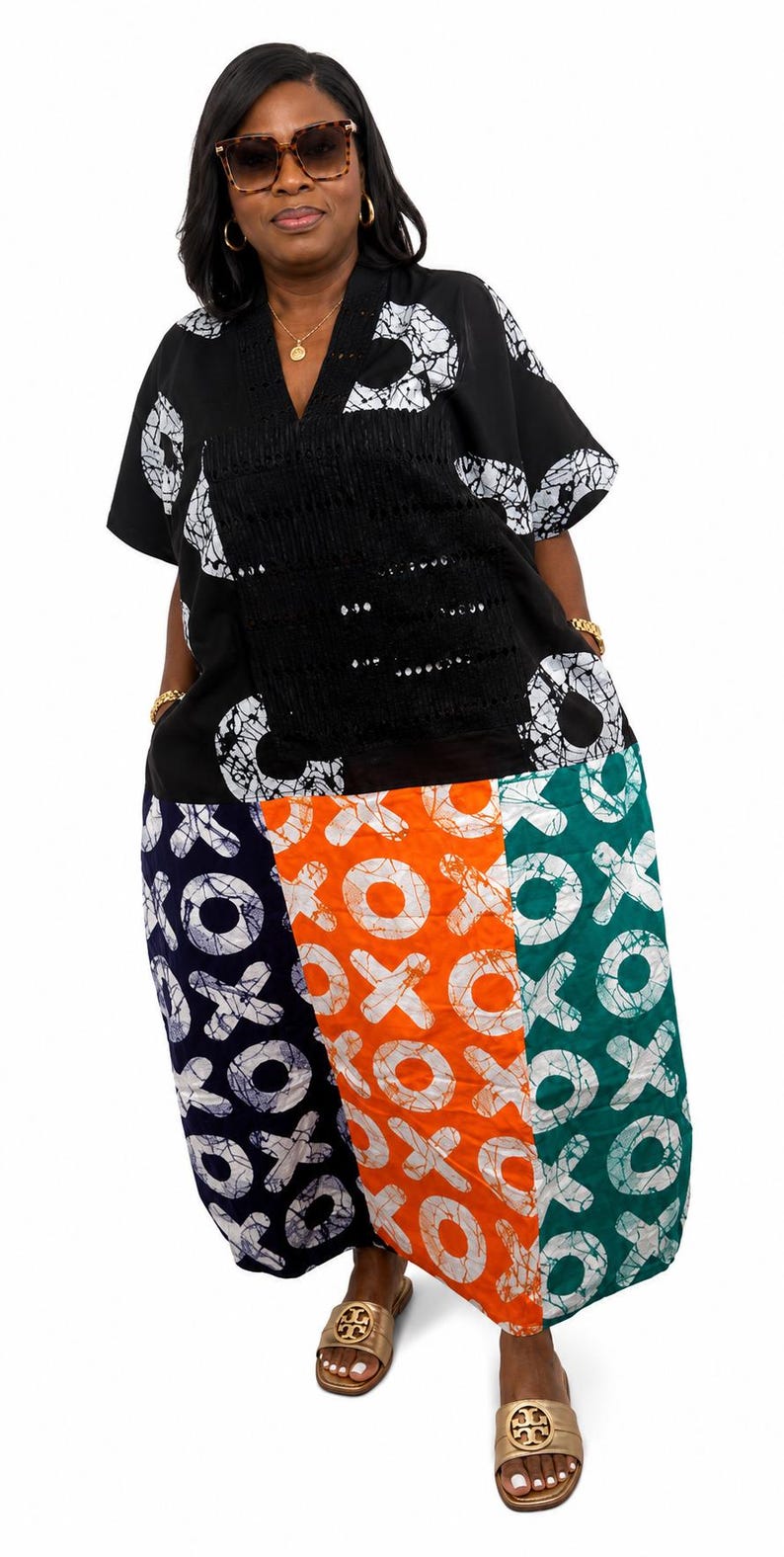 Pu&ograve; includere: Un abito a maniche corte con corpetto nero a motivi circolari bianchi e scollo a V. La gonna &egrave; divisa in tre pannelli verticali blu navy, arancione e verde, ciascuno decorato con un motivo bianco ripetuto a forma di XOXO.