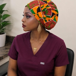 May include: A scrub cap featuring a vibrant geometric pattern in shades of orange, green, red, and black. The cap is worn with a deep purple V-neck scrub top that has a small pocket on the chest with the text FIGS clearly visible on a label.