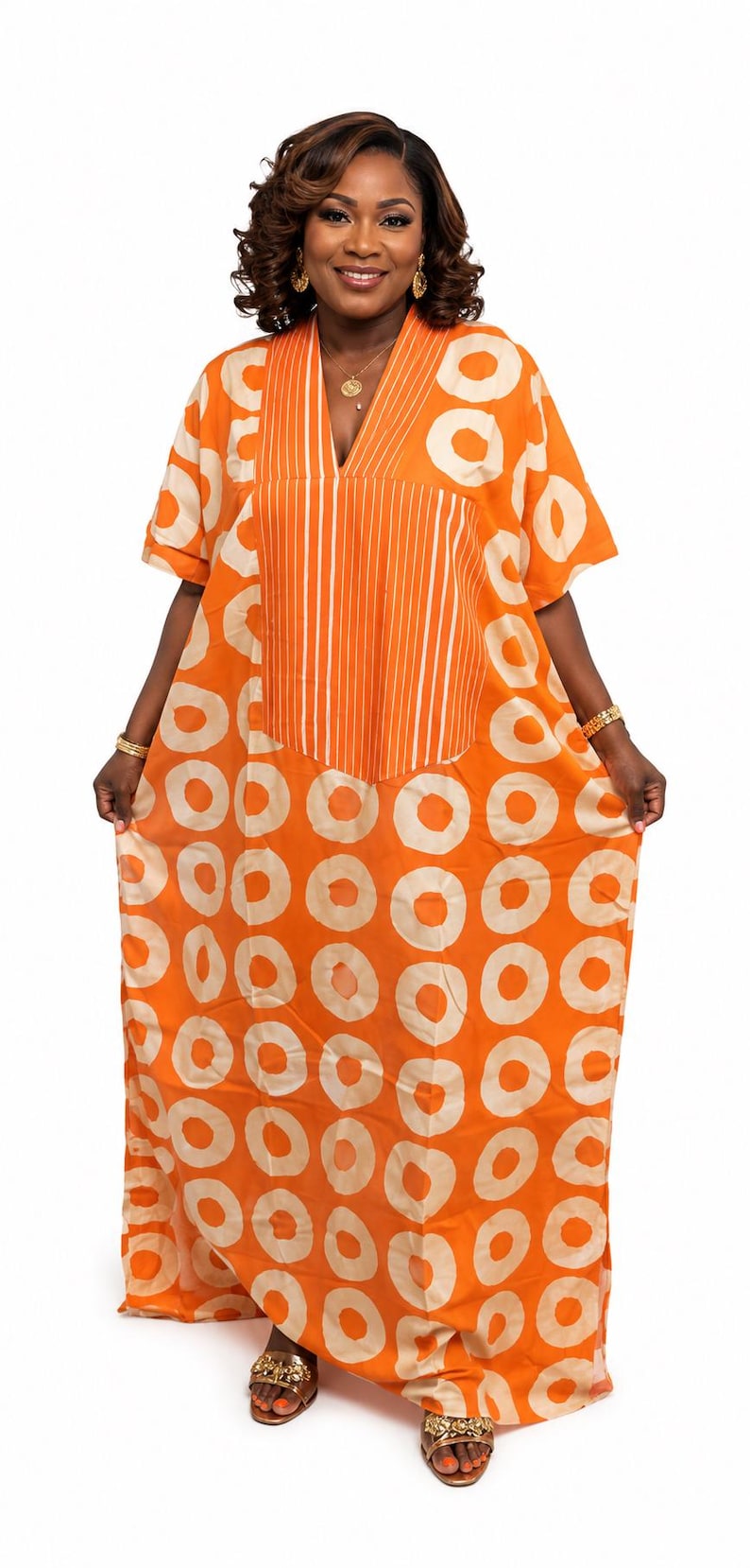 May include: A floor-length orange kaftan dress featuring a repeating pattern of large, light beige circles. The garment has short sleeves, a V-neckline, and a central vertical panel decorated with thin, white, parallel pinstripes running down the front.