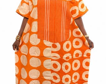 Könnte beinhalten: Ein leuchtend orangefarbenes Kaftan-Kleid mit einem sich wiederholenden Muster aus großen, hellbeigen Kreisen. Das Kleidungsstück hat einen V-Ausschnitt mit einem Mittelteil aus vertikalen weißen Streifen, kurzen Ärmeln und einer lockeren Silhouette.