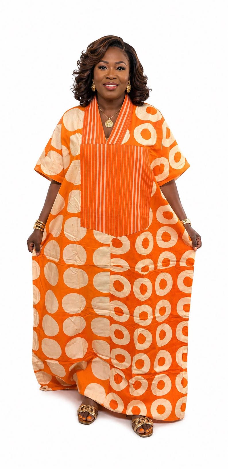 May include: A vibrant orange kaftan dress featuring a repeating pattern of large, light beige circles. The garment includes a V-neckline with a central panel of vertical white stripes, short sleeves, and a loose, flowing silhouette that reaches the floor.