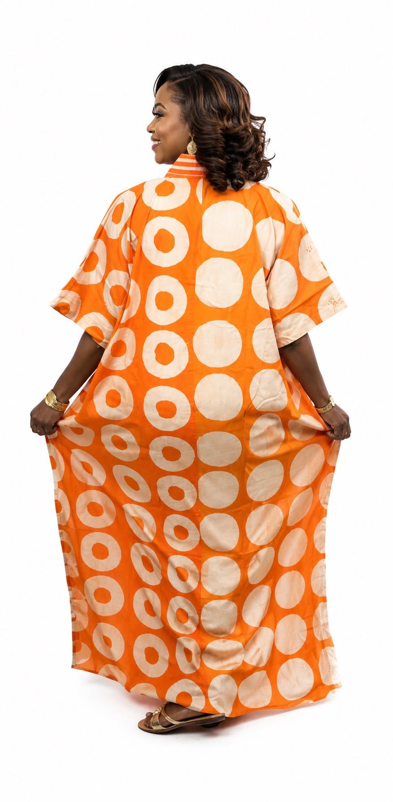 May include: A floor-length orange kaftan dress featuring a bold pattern of large, light cream-colored circles. The garment has short, wide sleeves, a high collar, and a loose, flowing silhouette that extends to the floor with a straight hemline.