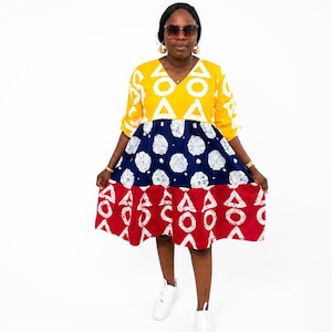 May include: A knee-length dress featuring three horizontal color-blocked sections. The top section is yellow with white triangle patterns, the middle is navy blue with white circular motifs, and the bottom is red with white triangle patterns.