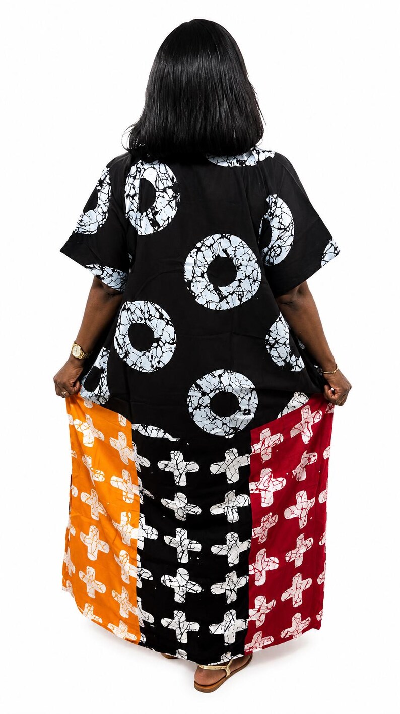 Pu&ograve; includere: Un abito caftano nero dal taglio ampio con un motivo batik circolare bianco sulla parte superiore e un pannello inferiore diviso in tre segmenti verticali di colore arancione, nero e rosso, decorati con un motivo a croce bianca.