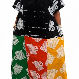 Pu&ograve; includere: Un abito caftano lungo fino ai piedi con corpetto nero, scollo a V e maniche corte, che prosegue con una gonna a blocchi di colore con pannelli verticali in verde, rosso e giallo, decorati con un motivo grafico bianco ripetuto.