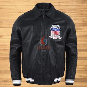 Könnte beinhalten: Eine schwarze Lederbomberjacke mit einem weißen und schwarzen Streifenbesatz an Kragen, Ärmelbündchen und Saum. Die Jacke hat einen Reißverschluss und einen Aufnäher auf der linken Brust mit der Aufschrift "AVIREX ESTABLISHED 1975".