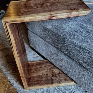 Puede incluir: Una mesa auxiliar de madera marrón oscuro con un diseño curvo único. La mesa tiene un acabado de madera natural y una superficie lisa.