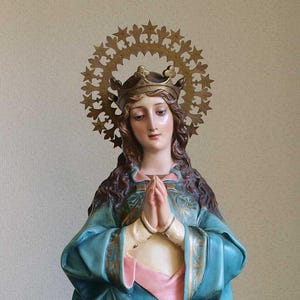 K&ouml;nnte beinhalten: Statue einer Frau mit Krone und Sternen-Heiligenschein. Sie tr&auml;gt ein blaues Gewand mit goldenen Verzierungen und hat die H&auml;nde zum Gebet gefaltet. Die Statue hat einen ruhigen Ausdruck.