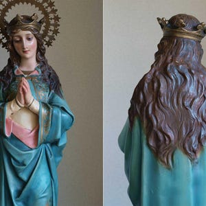 K&ouml;nnte beinhalten: Vintage Statue einer Frau mit Krone und Heiligenschein, die ein tealfarbenes Gewand mit rosa und goldenen Akzenten tr&auml;gt. Die Statue hat lange braune Haare und betet. Der Heiligenschein ist aus goldfarbenem Metall.
