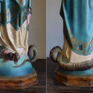 K&ouml;nnte beinhalten: Vintage Statuenfu&szlig; in T&uuml;rkis und Creme. Eine detaillierte Skulptur einer Schlange umkreist die F&uuml;&szlig;e der Figur. Die Kleidung der Statue hat goldene Akzente. Der Sockel ist aus Holz.