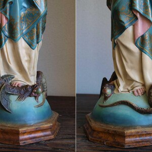 K&ouml;nnte beinhalten: Vintage Statue, die eine Figur in flie&szlig;enden Gew&auml;ndern darstellt, mit einem Schal mit t&uuml;rkisfarbenem und goldenem Muster. Die Statue steht auf einem Sockel mit einer sich darum windenden Schlange. Der Sockel ist in Blau- und Braunt&ouml;nen bemalt.