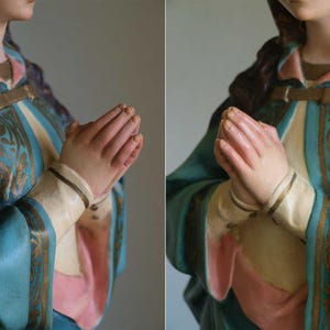 K&ouml;nnte beinhalten: Statue einer Figur mit zum Gebet gefalteten H&auml;nden. Die Figur tr&auml;gt eine t&uuml;rkisfarbene Robe mit goldenen Akzenten und ein rosa-cremefarbenes Untergewand. Die Statue hat lange, dunkle Haare.