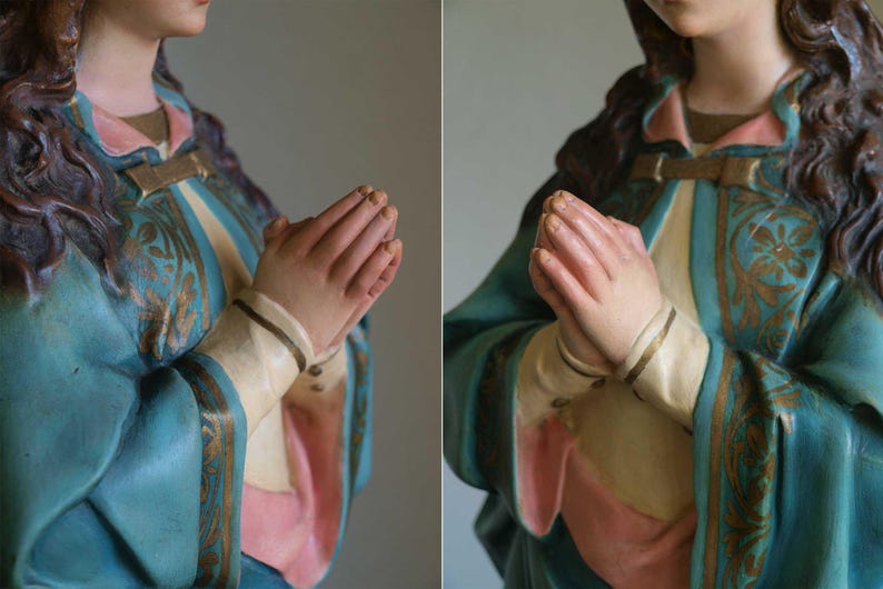 K&ouml;nnte beinhalten: Statue einer Figur mit zum Gebet gefalteten H&auml;nden. Die Figur tr&auml;gt eine t&uuml;rkisfarbene Robe mit goldenen Akzenten und ein rosa-cremefarbenes Untergewand. Die Statue hat lange, dunkle Haare.