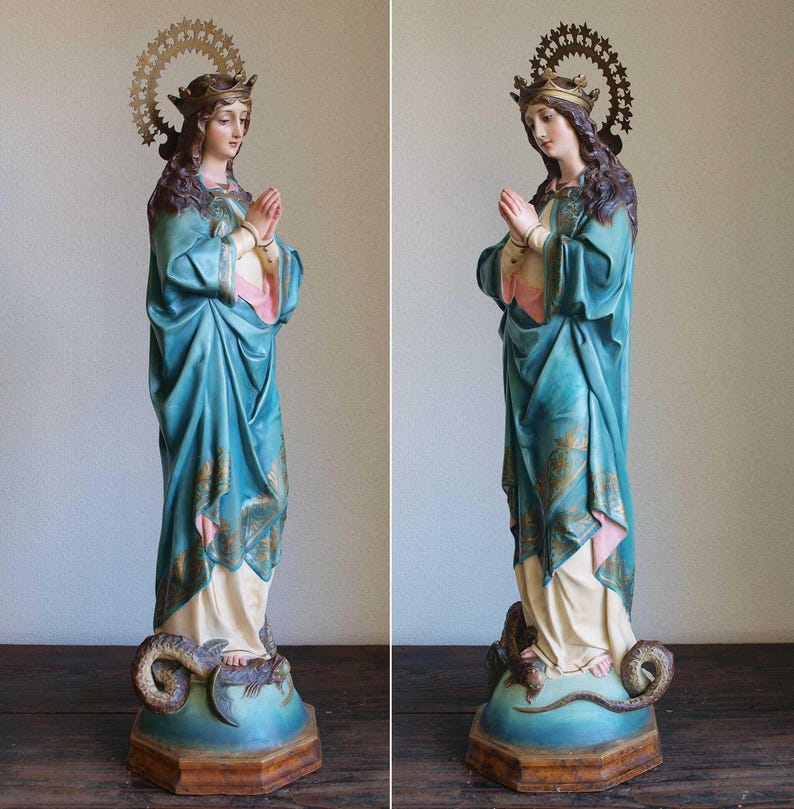 K&ouml;nnte beinhalten: Detaillierte Statue einer Frau in einem flie&szlig;enden tealfarbenen Gewand, die H&auml;nde zum Gebet gefaltet. Die Statue hat eine goldene Krone und einen Heiligenschein und steht auf einem Sockel mit einer Schlange. Die Statue ist etwa 76 cm hoch.