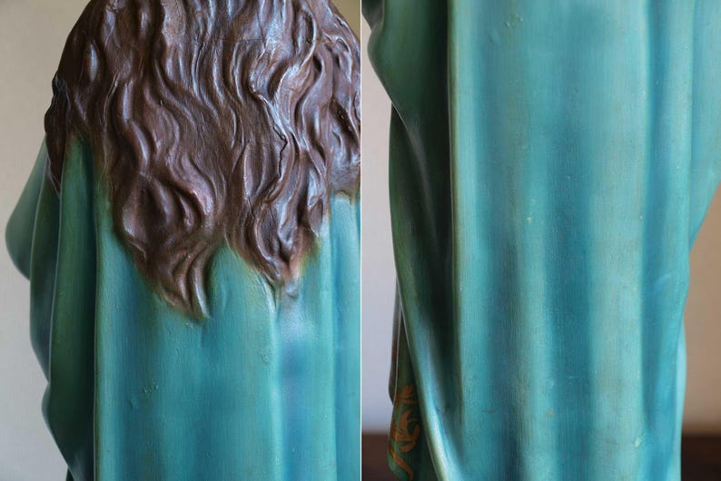 K&ouml;nnte beinhalten: Detailansicht einer Statue, die den R&uuml;cken von Kopf und Schultern zeigt. Die Statue hat langes, welliges braunes Haar und ein teal-farbenes Gewand. Der Stoff weist subtile Farb- und Texturvariationen auf.
