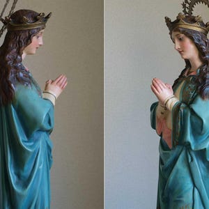 K&ouml;nnte beinhalten: Vintage Statue einer Frau in einem tealfarbenen Gewand, die H&auml;nde zum Gebet gefaltet. Die Statue hat eine goldene Krone und einen Sternenkranz. Die Frau hat lange braune Haare und einen ruhigen Ausdruck. Ein religi&ouml;ses Objekt.