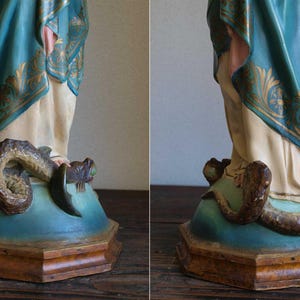 K&ouml;nnte beinhalten: Eine Vintage-Statue mit einer Figur in flie&szlig;enden Gew&auml;ndern, mit t&uuml;rkisfarbenen und goldenen Akzenten. Die Figur steht auf einem Sockel mit einer sich darum windenden Schlange. Der Sockel ist t&uuml;rkis und braun, mit detailliertem, gealtertem Aussehen.