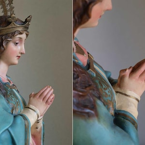 K&ouml;nnte beinhalten: Detaillierte Statue einer Frau mit Krone und Heiligenschein, die ein tealfarbenes Gewand mit goldenen Akzenten tr&auml;gt. Ihre H&auml;nde sind zum Gebet gefaltet. Die Statue hat einen ruhigen Ausdruck und ist mit realistischen Hautt&ouml;nen bemalt.